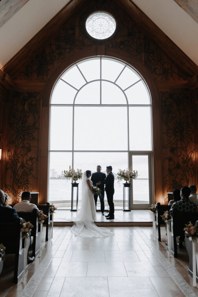 Dark ornate wood paneling behind wedding couple getting married with large ocean facing window