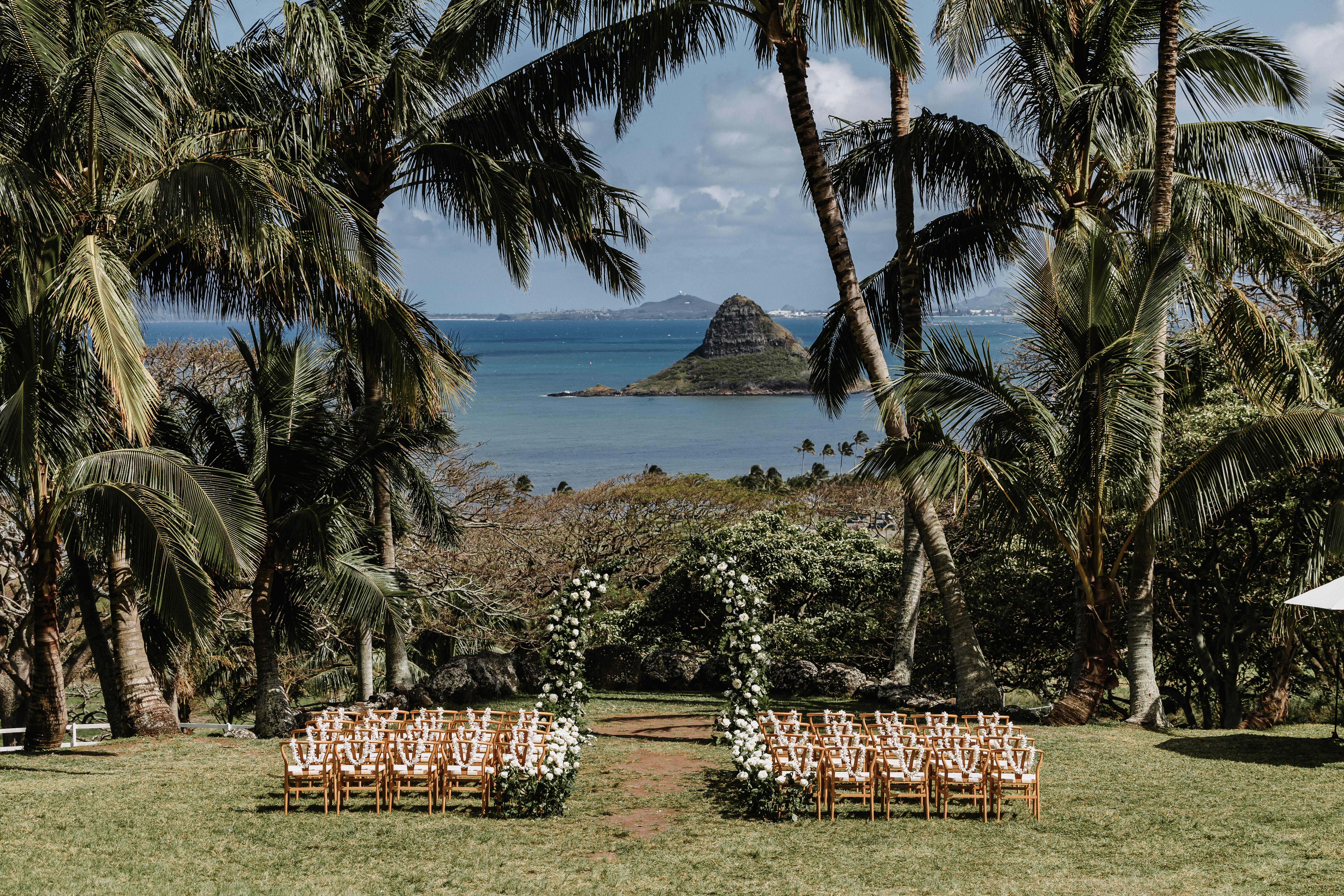 View from the top of the mountain looking down at a ceremony set up and palm trees in front of China man's hat and the ocean.