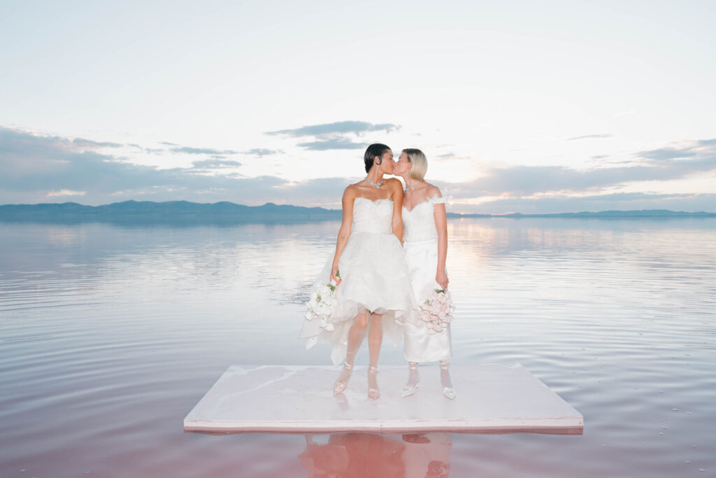 Two brides kissing during a wedding photo shoot at Pink Lake in Utah, captured by a destination wedding photographer