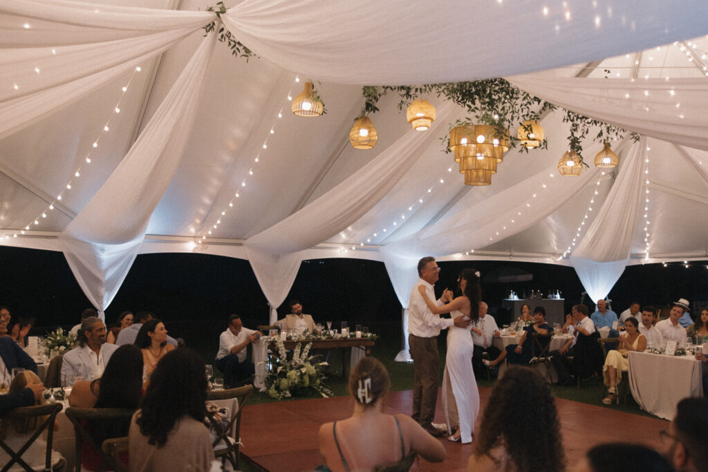 Bride dancing with her father under string lights during a tented wedding reception at Kualoa Ranch Paliku Gardens
